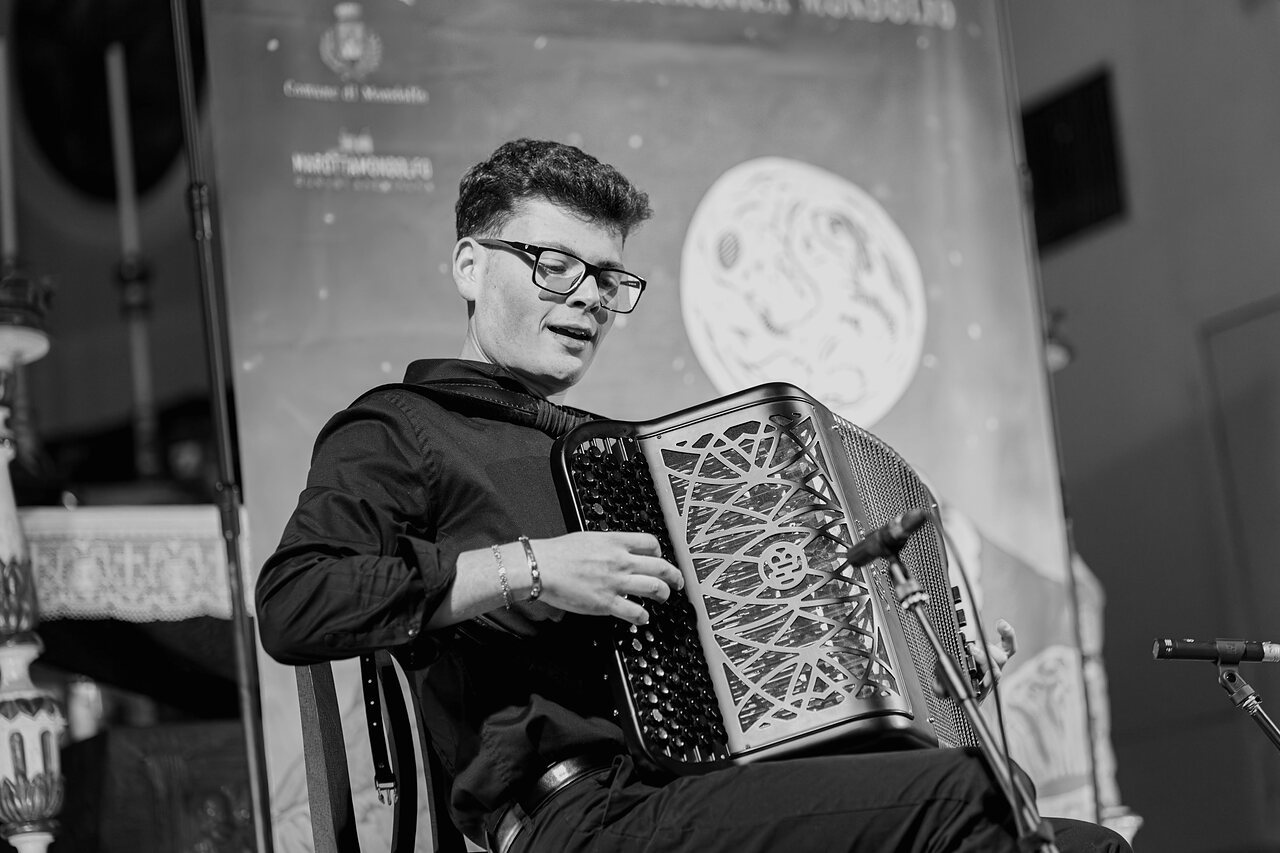 Francesco Scarselli playing his Bugari accordion, the festival backdrop lit behind him